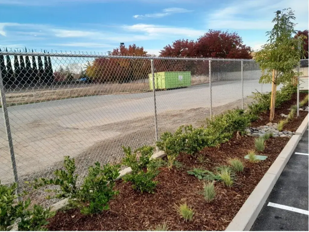 A chain-link fence along a commercial property with well-maintained landscaping.