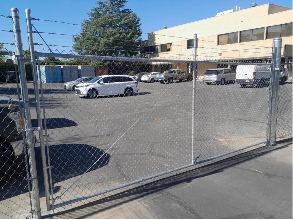 A chain-link fence with a gate, providing security to a parking lot with parked vehicles.
