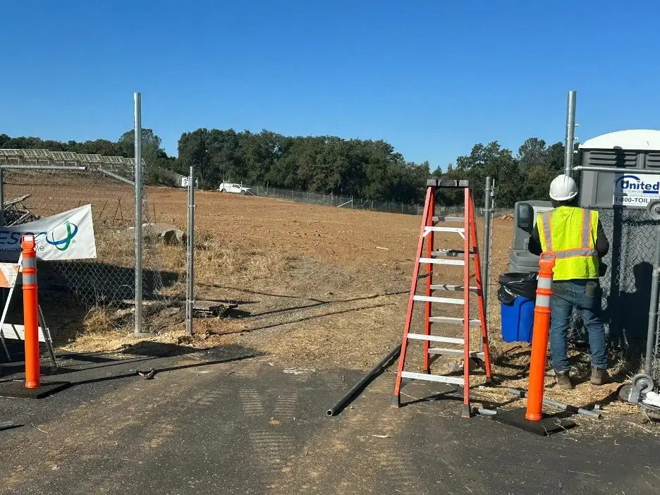 A worker in a yellow vest near a temporary fence at a construction site.