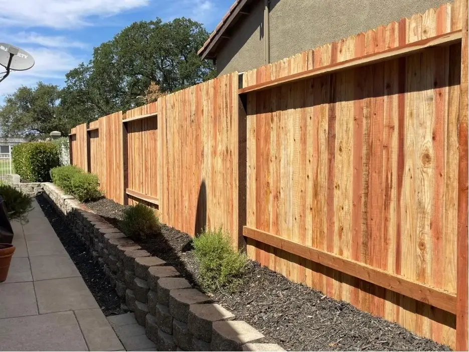 A wooden privacy fence with decorative scalloped top, enclosing a landscaped area.