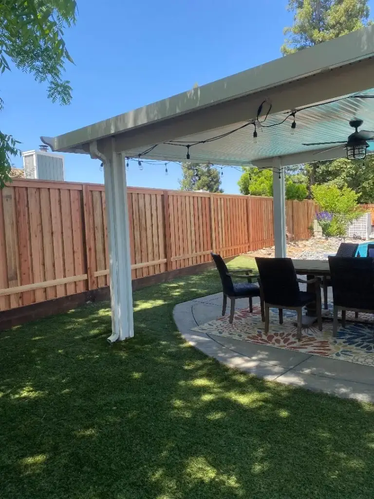 A patio with a newly installed wooden fence, surrounded by lush green grass and clear blue skies.