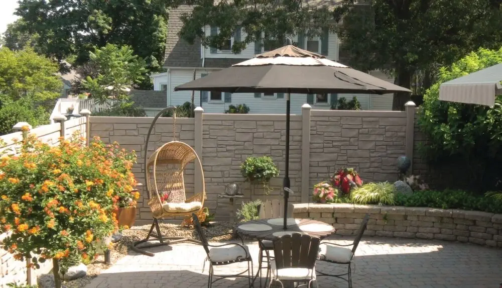 A peaceful patio with a stone wall, umbrella, and greenery, perfect for relaxation.