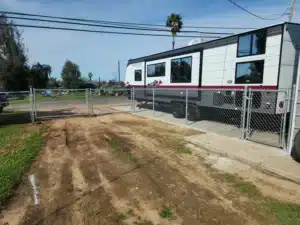 Galvanized chain link fence with a gate is installed next to a large campsite trailer, representing a longest lasting fence type choice.