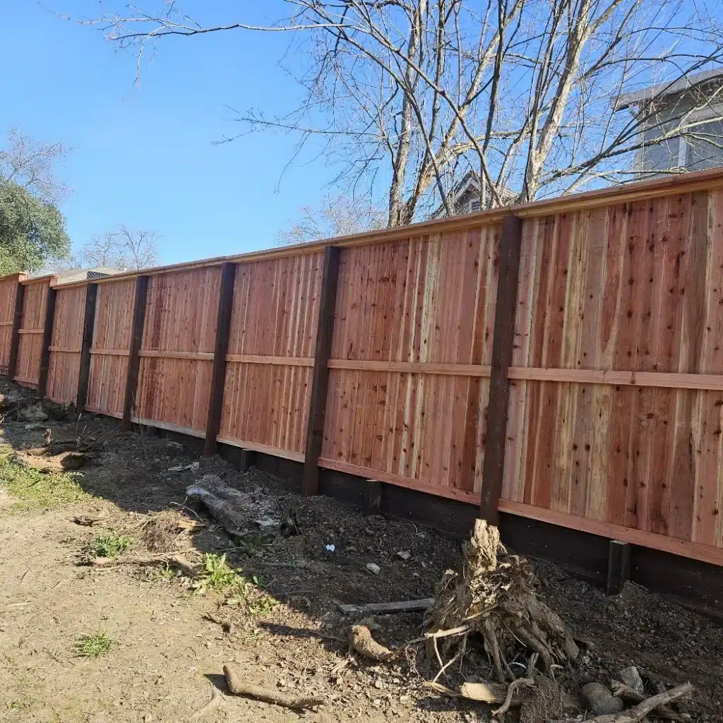 Close-up of a new wood Residential Fence with dark posts on a sloped yard.
