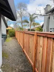 Tall wooden privacy fence running down a residential gravel path; this is an ideal fence height for secluding the area.