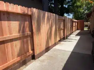 Redwood pickets installed with a dark pressure-treated kickboard to create a secure Taller Wood Fence along a walkway.