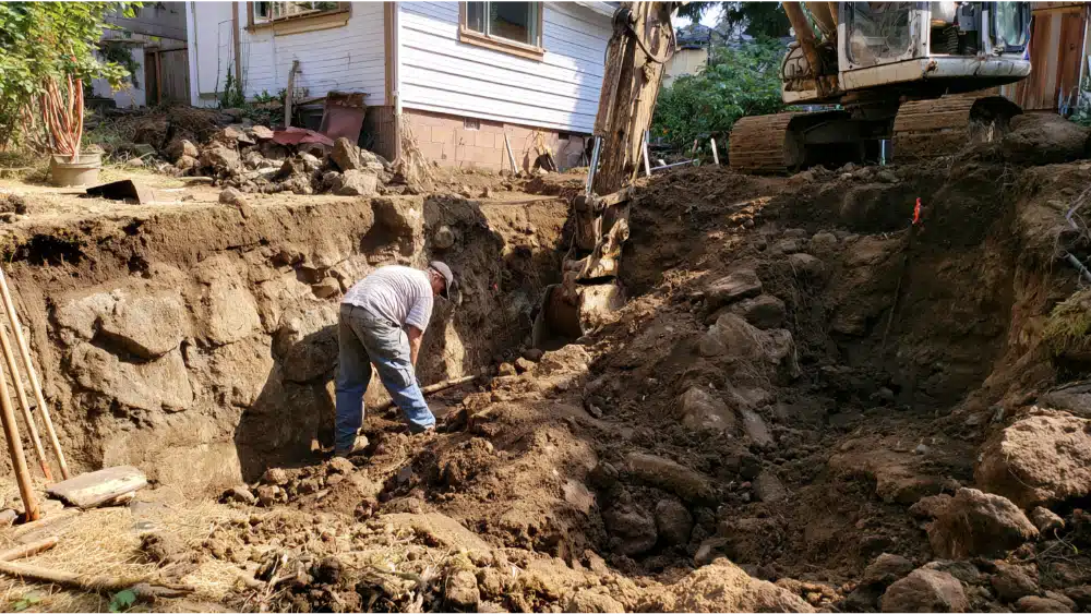 Contractors installing helical tieback anchors to stabilize a leaning retaining wall under soil pressure.