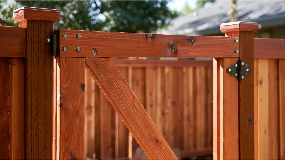 Wood gate frame reinforced with diagonal bracing, corner brackets, fasteners, and heavy-duty hinges.